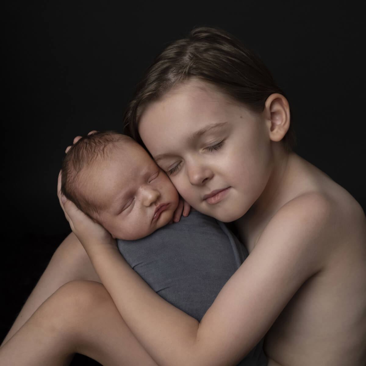 After: Boy holding a sleeping newborn against a black background