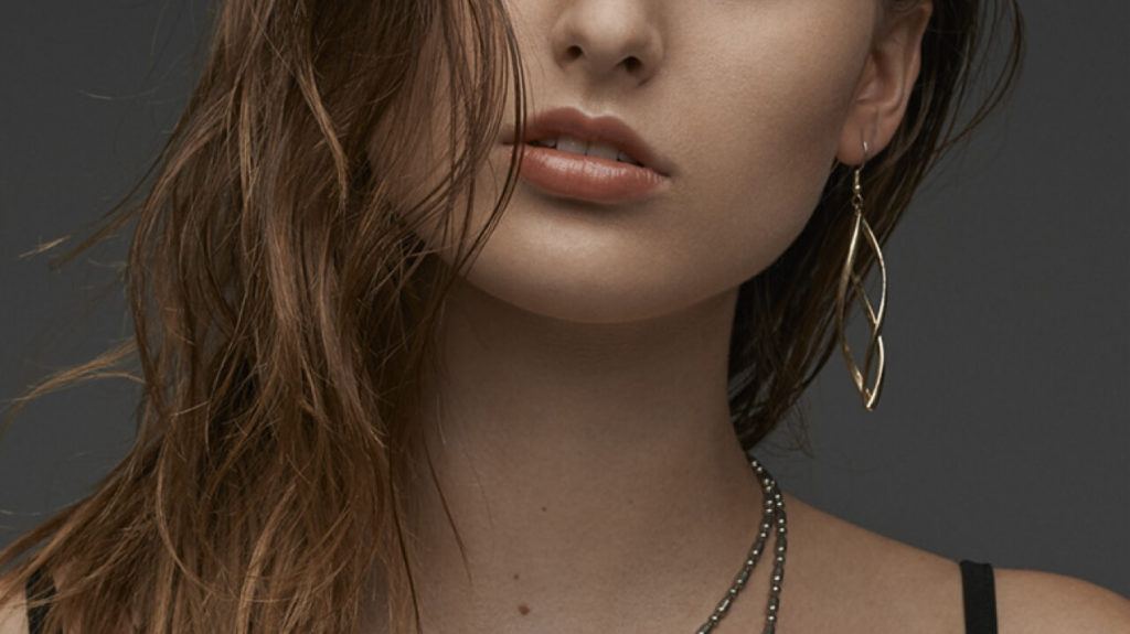 Close-up of a woman’s lips and chin with a drop earring on a dark grey background