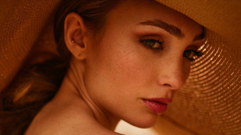 Close-up portrait of a woman in a wide straw hat, in warm orange tones